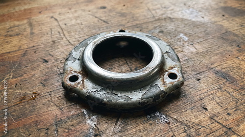 Used coil spring upper mount plate with peeling paint and rust on a wooden workbench