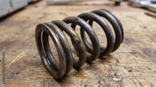 Used rusty and oily automotive engine valve spring resting on a dirty wooden workbench
