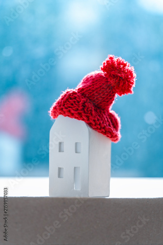 A small model house wearing a colorful knitted hat sits on a table. Improve energy efficiency during the ongoing energy crisis.