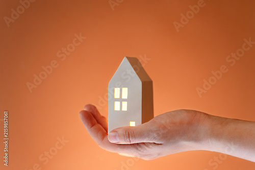 A person holds a small model of a house in their hand. House has lights shining from its windows. Real estate. Renting or buying a house.