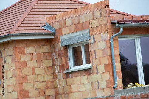 Une maison individuelle en cours de construction, réalisée en briques alvéolaires, avec une toiture en tuiles terre cuite et des menuiseries extérieures déjà posées.
