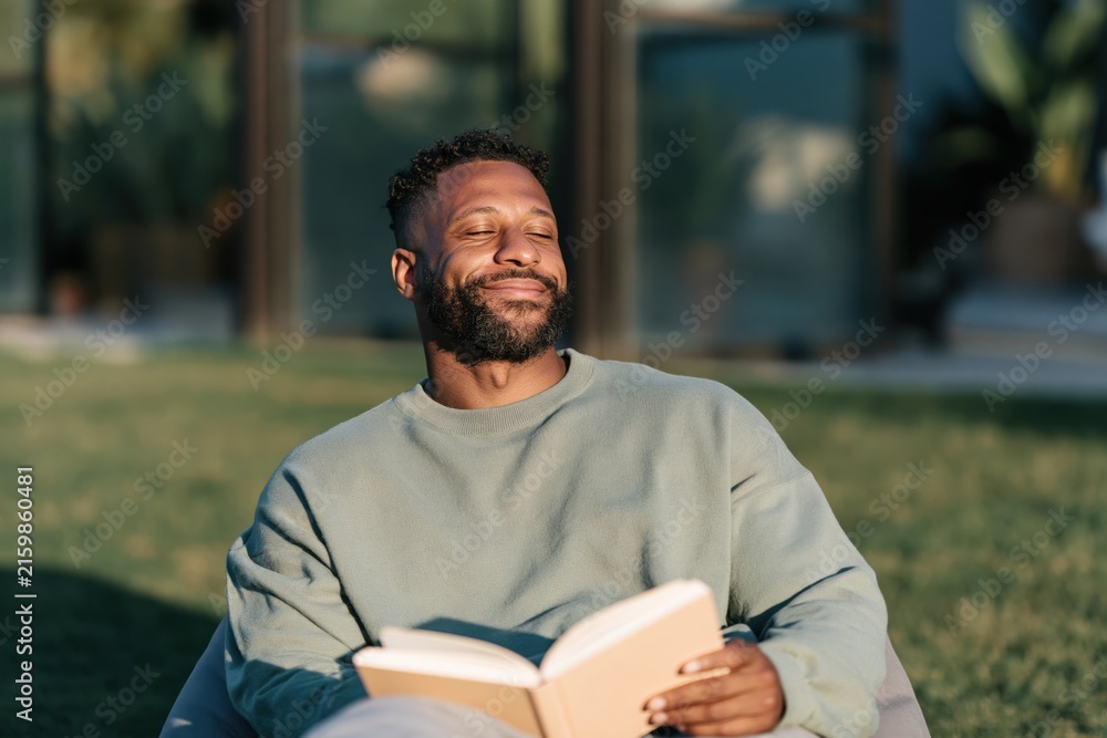 Fototapeta premium Relaxed man sunbathing outdoors with book portrait for lifestyle background and mindfulness banner design