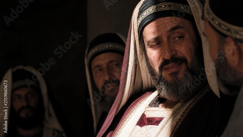 Smiling Pharisee in ancient religious clothing surrounded by fellow Jewish leaders. Biblical drama illustrating hypocrisy, social judgment, wealth, and hidden motives from the Gospel of Luke.