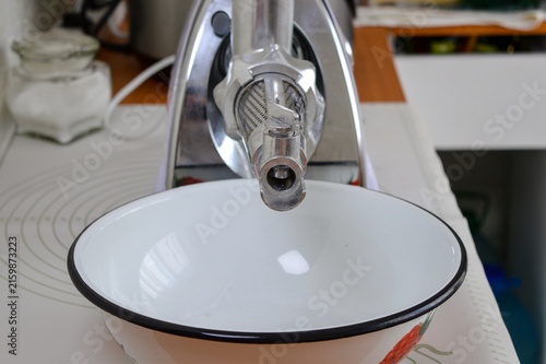 Obraz na płótnie Front view of electric meat grinder with juicer squeezer attachment over enamel bowl close-up