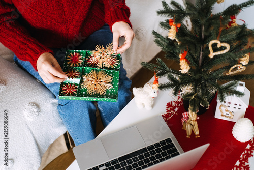 Quadro su tela Woman holds box with straw star ornaments on lap beside laptop and small decorated tree
