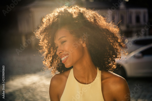 Canvas Print Smiling woman with curly hair bathed in warm sunlight, outdoor portrait capturin
