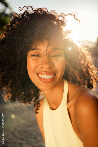 Canvas Print Smiling young woman with curly hair enjoying golden hour sunlight in an outdoor