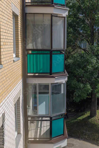 Enclosed glazed balcony with green panels on the facade of a residential apartment building. Concept of balcony renovation, housing modernization and energy efficient glazing.