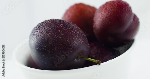 Ripe, juicy plums in a snow-white bowl. Fruits and time of harvesting. Juicy plums sprinkled with water close up.