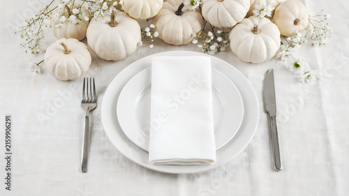 Elegant autumn table setting with white pumpkins and a plate with a napkin and silverware for a festive dinner party