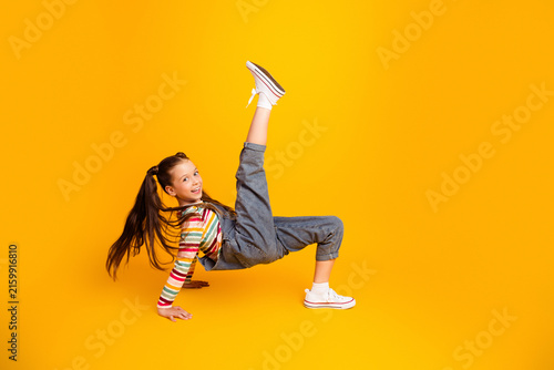 фотографія Smiling girl breakdancing in denim overalls and striped shirt on bright yellow b
