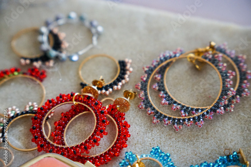 Close-up collection of handcrafted beaded hoop earrings in red, blue, and pink tones arranged on a soft textile surface, suitable for fashion, jewelry, artisan, and accessory marketing.