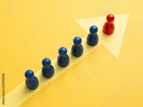 Red Game Piece Leading Blue Pieces on a White Arrow Over a Yellow Background Representing Leadership and Direction
