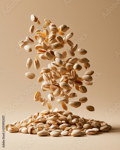 Pistachio nuts falling in dynamic motion on beige background.