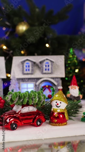 An orange car with a Christmas tree on its roof drives past the Christmas village