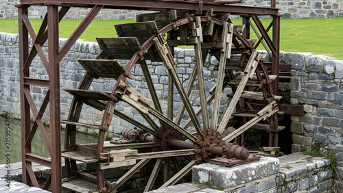 Historic wooden water wheel mechanism set in stone landscape for traditional milling and sustainable energy generation heritage display
