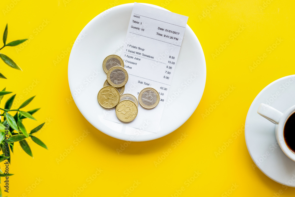 Fototapeta premium Pay restaurant bill by cash. Reciept and coins on plate on yellow background top view