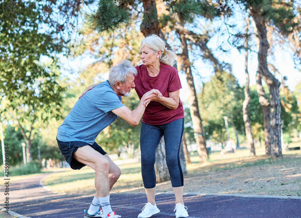 Fototapeta premium Active mid age senior mature couple jogging together, helping and supporting each other with a injury problem in the park