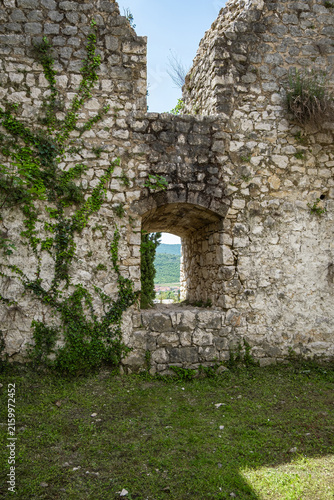 Quadro su tela Weathered stone fortress ruins with ivy covered walls and arched doorway overloo