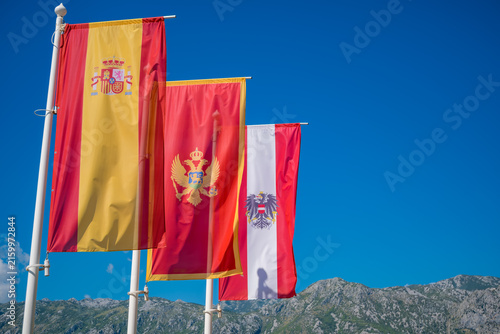 Obraz na płótnie Spanish, Montenegrin and Austrian flags waving on white poles against rugged mou