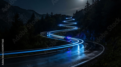 A long-exposure photograph at night captures a winding mountain road with bright blue light trails from a vehicle moving along it.