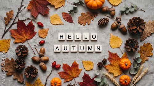 Flat lay composition with the text hello autumn surrounded by colorful fall leaves pine cones and small pumpkins on a rustic grey wooden background