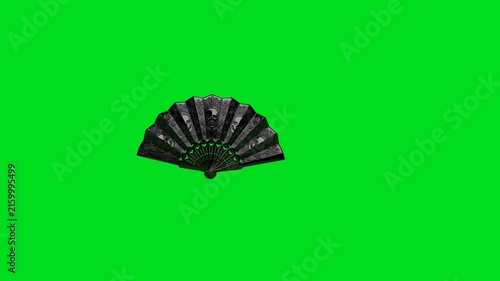 A detailed black folding fan with skull patterns on a vibrant green background