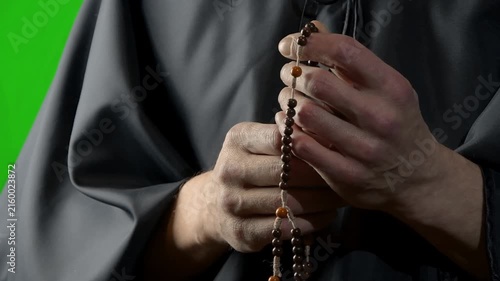 Monk slowly counting wooden prayer beads in close-up against green background