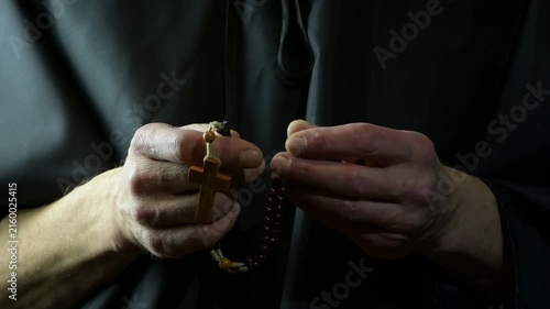 Monk slowly moves wooden rosary beads with cross during quiet prayer