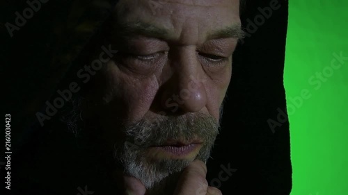 Closeup of hooded monk lowering gaze and touching beard thoughtfully