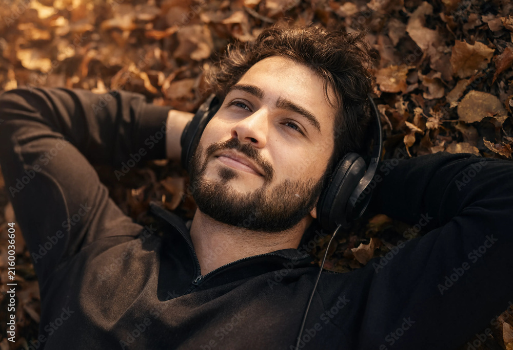 Fototapeta premium A happy man in jeans walks in an autumn park and listens to music on headphones.