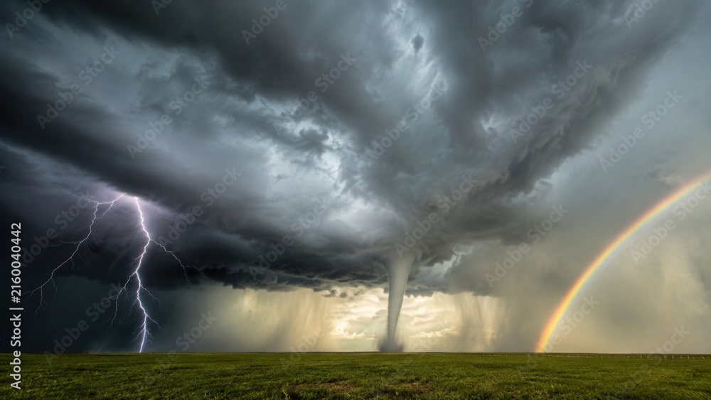 Fototapeta premium Powerful tornado with lightning strike and rainbow beneath dramatic storm clouds over open green landscape