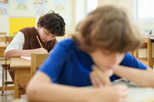 Принти на полотні Focused elementary student writes during a classroom exam while classmates work quietly, reflecting concentration, academic assessment, and everyday school learning