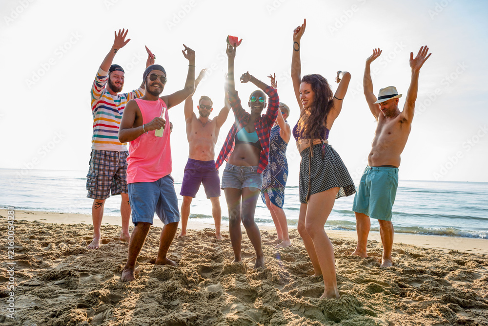 Obraz premium Group of friends dancing joyfully on a sunny beach.