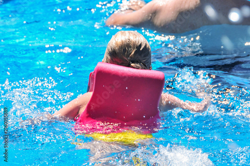 Foto Young girl in a pink life preserver swims through bright blue pool water toward an adult, illustrating flotation safety, water safety, supervised swimming, and child protection