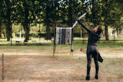Fotografie Woman archer holding longbow aiming at target outdoors