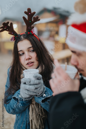 Fotografie Young friends share warm cups at an outdoor Christmas market in winter