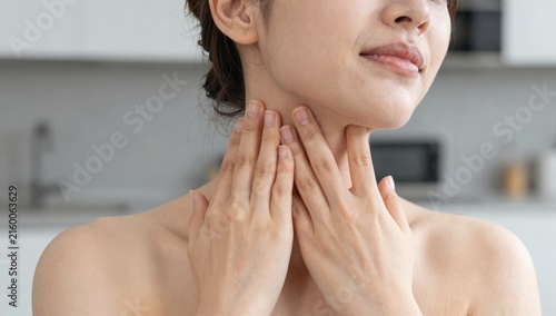 Young woman holding her neck in pain and discomfort at home, grimacing from neck ache and tension while seeking relief and self-care in a bright modern living space