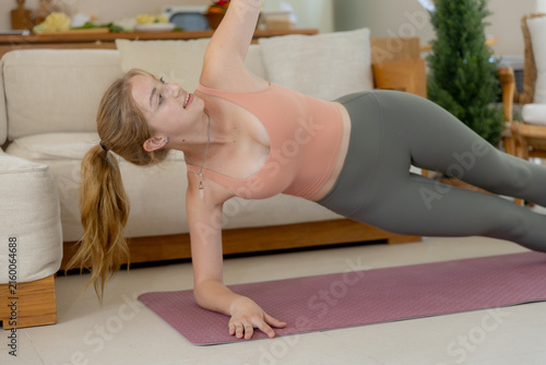Canvas Print Young woman practicing fitness exercise at home doing side plank on yoga mat in