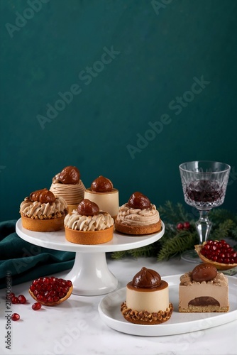 Candied chestnut pastries on a white cake stand. Festive Mont Blanc desserts with cream and chestnuts on a dark green background