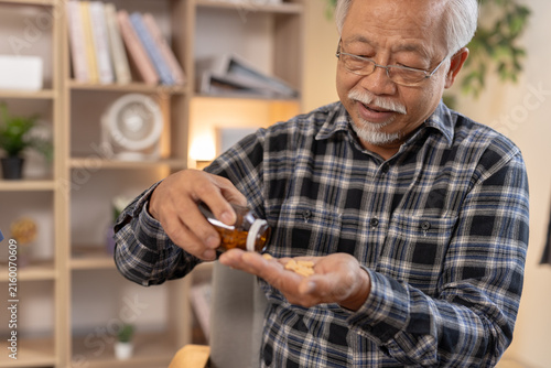 фотографія Senior asian man pouring medicine pill from brown bottle into hand for daily hea