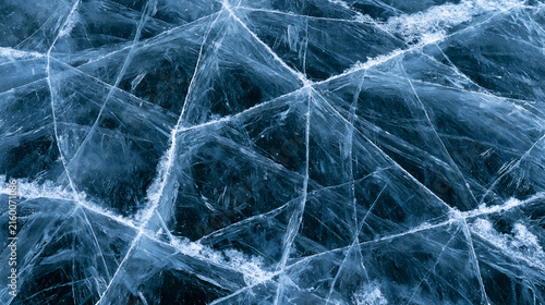 Intricate deep blue ice fractures forming a web-like pattern across a frozen lake. Captivating natural background for winter conceptual imagery.