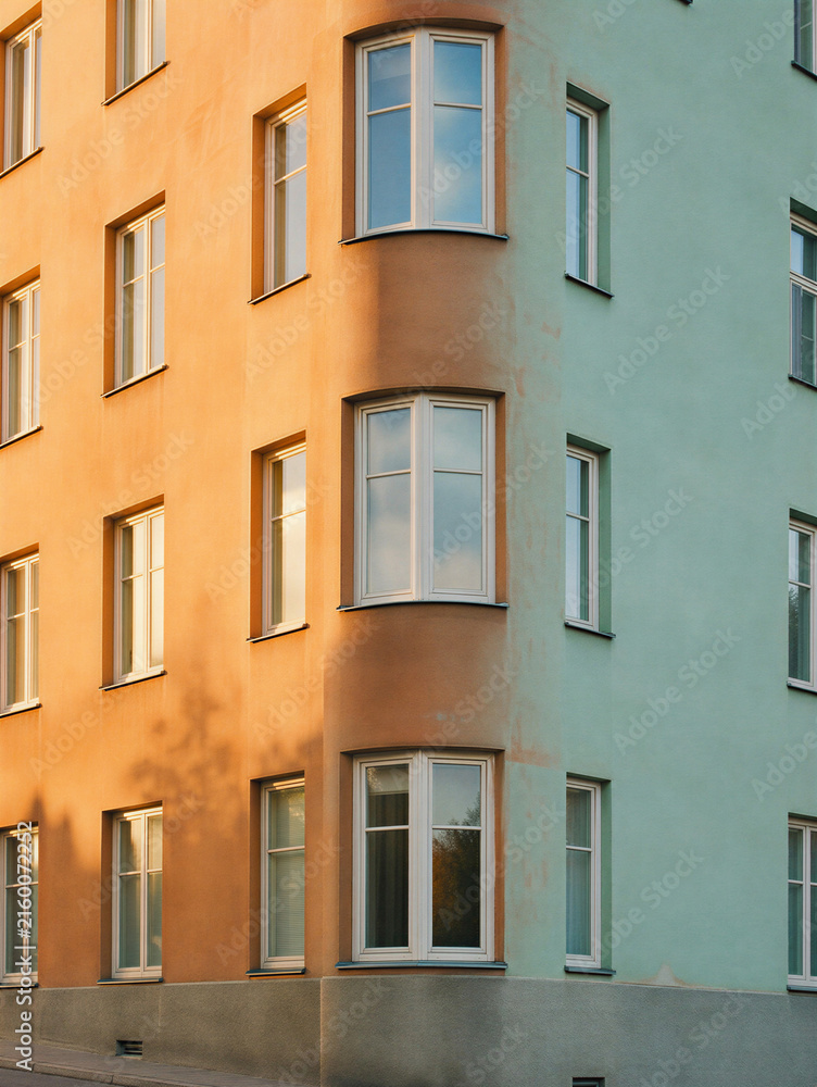 Obraz premium Vertical photo of a colorful residential building corner with curved windows. Orange and green painted apartment facade in sunlight