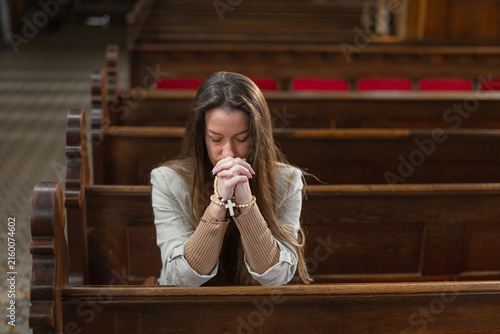 A woman is praying alone in a European Catholic church during Holy Mass. She shows devotion and faith through her prayer.