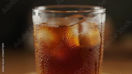 Extreme close-up of a refreshing iced dark beverage, such as cola or iced tea, sweating with condensation and filled with ice cubes in a tall glass.