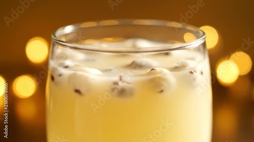 Festive Close-Up of Refreshing Yellow Cocktail Garnished with Floating Ingredients Against a Warm Golden Bokeh Background, Ideal for Holiday Parties or Celebrations.