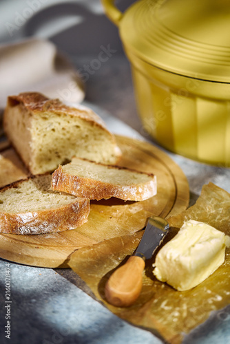 Close-up of a freshly baked artisan loaf cut in half, revealing porous crumb structure. Stacked on a wooden board with butter and linen cloth nearby.