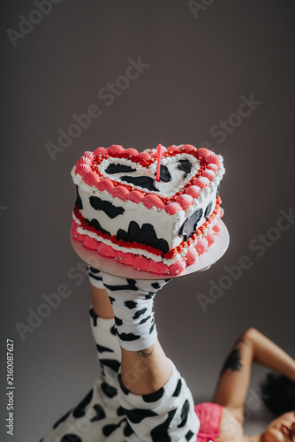 Obraz na plátne A heart-shaped birthday cake with pink frosting and a single candle held aloft by raised legs