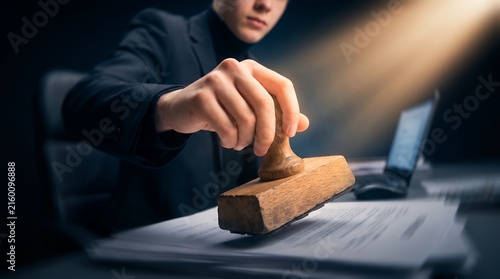 Businessman stamping official documents showcasing wooden stamp tool, contract paper and office environment, concept for legal authorization and agreement approval