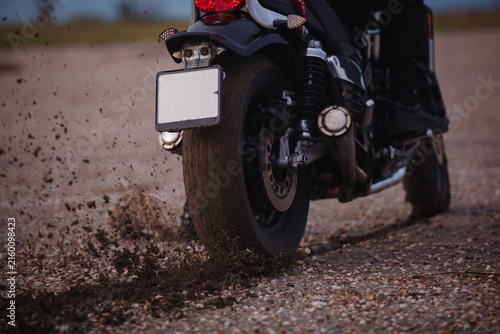 Close up of motorcycle rear wheel spinning and spraying dirt and gravel on ground. Power acceleration, offroad traction and tire burnout action concept